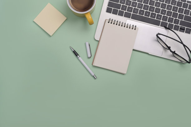 笔记本电脑，记事本，眼镜，咖啡杯和绿色背景上的便签。前视图。图片下载