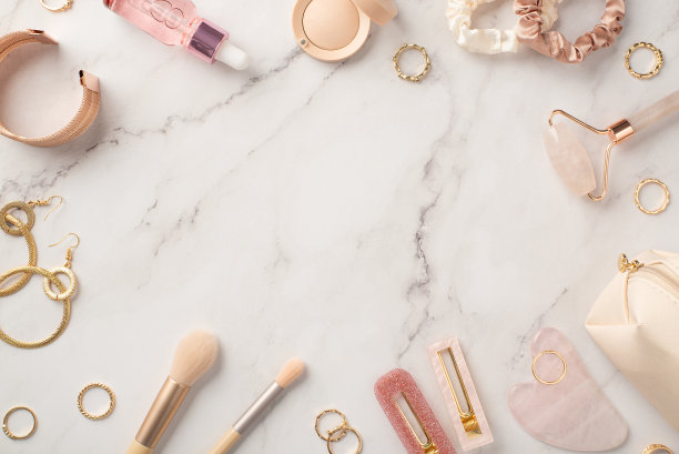 顶部照片的粉红色发夹玫瑰石英滚轮挂沙玻璃瓶眼影发圈金耳环戒指腕带和化妆包在白色大理石背景与copyspace在中间图片下载