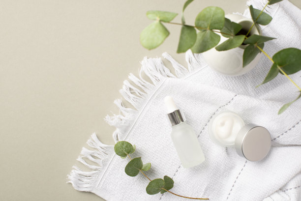 天然化妆品的概念。透明滴瓶奶油罐与银盖白色毛巾和桉树在孤立粉彩灰色背景与copyspace的顶部视图照片图片下载