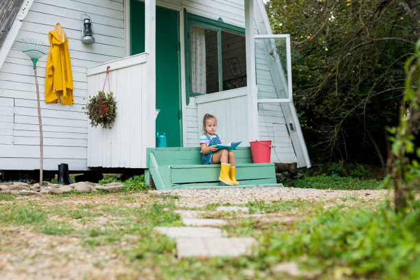 可爱的小女孩坐在台阶上，在后院看书。幼儿独立阅读的发展。农村图片下载