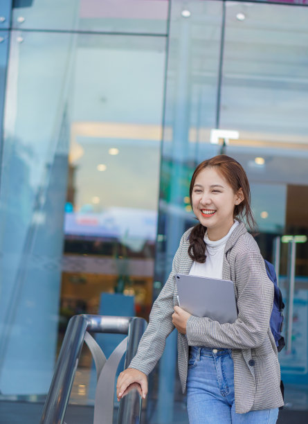 一名亚洲女学生在课间拿着平板电脑站在商场前，想着在外面通过互联网学习。图片下载