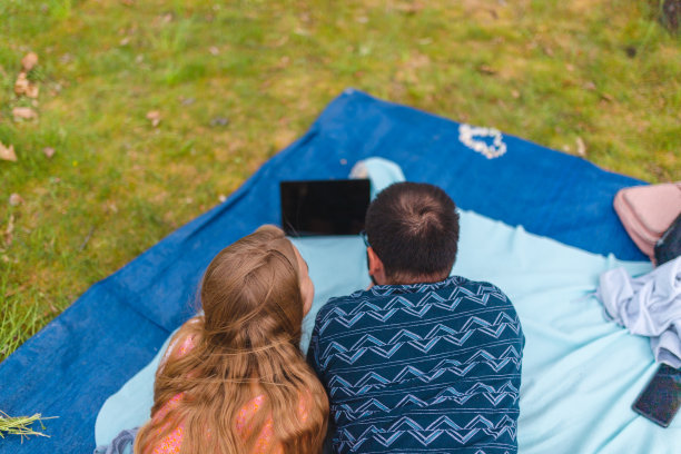 从上往下看，一对年轻夫妇使用平板电脑，而躺在野餐毯子在自然图片下载