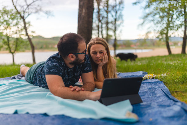年轻浪漫的夫妇躺在野餐毯子上，在平板电脑上看电影，而在自然图片下载