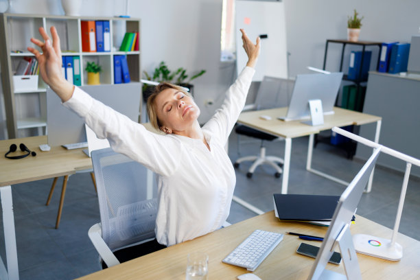 成熟的商业女性在久坐的工作结束后，坐在办公室的办公桌前做伸展运动图片下载