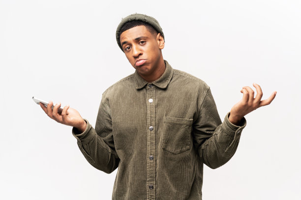 有魅力的男人穿着休闲衬衫，手持智能手机，张开双手，不知道如何使用应用程序。室内工作室拍摄图片下载