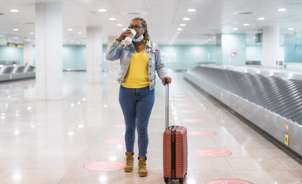 一名非洲妇女一边喝着咖啡，一边拿着行李走进机场航站楼图片下载