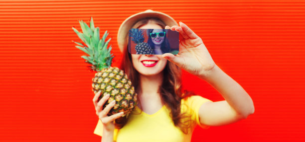 夏天肖像特写快乐微笑的女人与菠萝采取自拍智能手机戴草帽，太阳眼镜在生动的背景图片下载