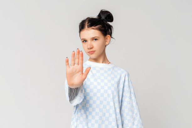 求你了，不要，停下来。严肃的黑发少女，站在浅灰色的背景下，穿着时髦的t恤，看着镜头，伸出手臂示意停止。呆在家里。社会距离图片下载