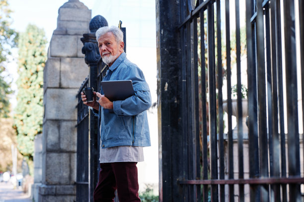 一名大四学生拿着咖啡和笔记本电脑走出了教学楼。图片下载