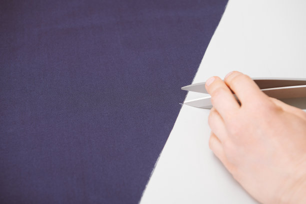 裁缝在桌子上用剪刀裁剪蓝色布料图片下载