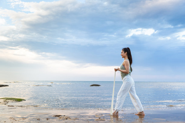 年轻的女士练习伸展使用一个阻力带在海滩-股票照片图片下载