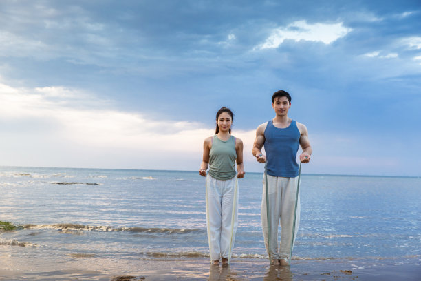 一对年轻夫妇在海滩上用阻力带做瑜伽拉伸-照片图片下载