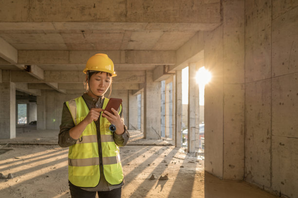 在阳光明媚的工地上，一位女工人拿着手机图片下载