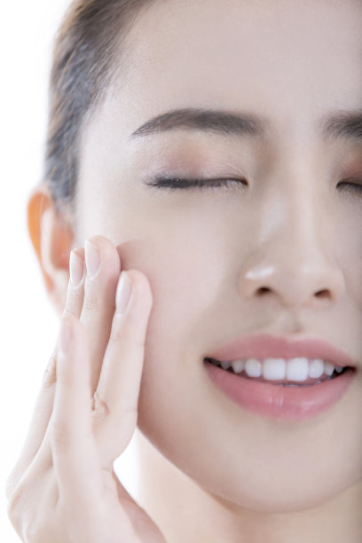 在白色背景照片上，一位刚刚用过护肤品的年轻女士闭着眼睛抚摸着她光滑的皮肤图片下载