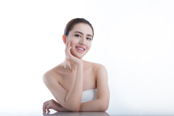 美丽的年轻女士怀抱她的下巴和微笑，因为她喜欢她的美容例行，在白色背景-股票照片图片下载