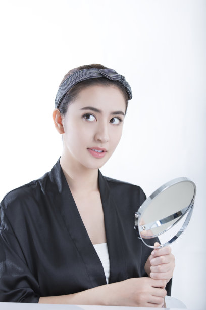 一位优雅、年轻、美丽的中国女士正看着镜子里的自己，白色背景照片图片下载