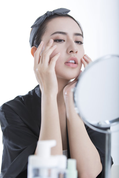 美丽的年轻中国女人使用护肤品在化妆镜前，在白色背景-股票照片图片下载