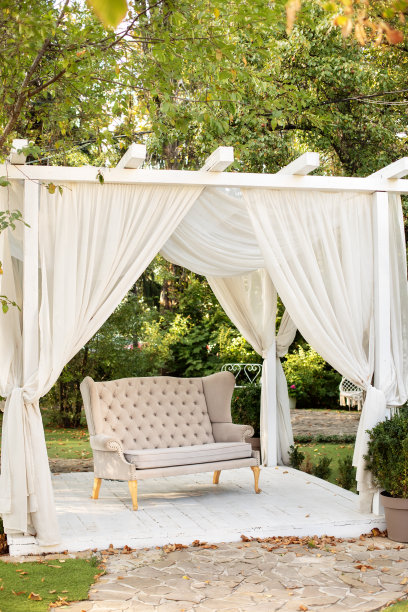 婚礼装饰。带有白色窗帘的夏日凉亭。浪漫的凹室。装饰户外露台。户外休闲凉亭。在花园里有一个讲台，上面放着普罗旺斯风格或乡村风格的沙发图片下载