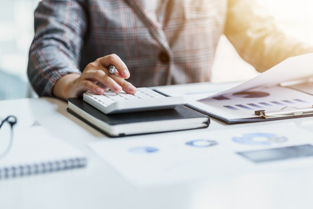 特写一位在现代办公室里使用计算器和持有会计图表数据纸做数学金融的女商人。图片下载