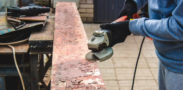 一个男人正在磨一块木板。清除木板上的旧漆。木工工作。图片下载