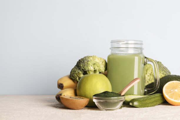 绿色果汁玻璃瓶，螺旋藻粉，蔬菜和水果蓝色背景。健康、生食、纯素饮食的概念。本空间图片下载