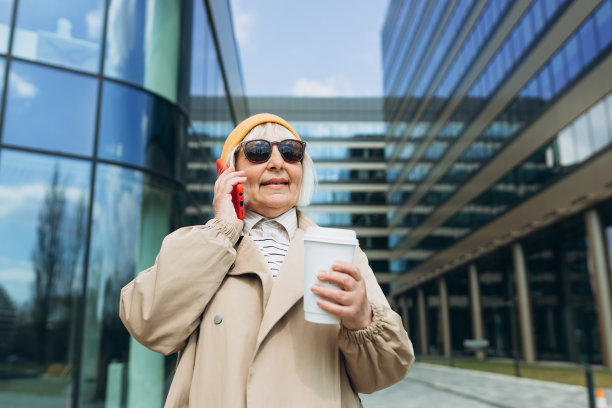 有吸引力的女商人喝咖啡和使用电话，业务上的想法。成功的商业女性在黄色帽子和太阳镜讲电话和步行与纸生物杯图片下载