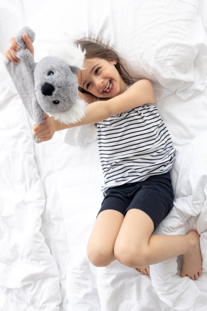 快乐的小女孩和柔软的玩具考拉在床上。图片下载