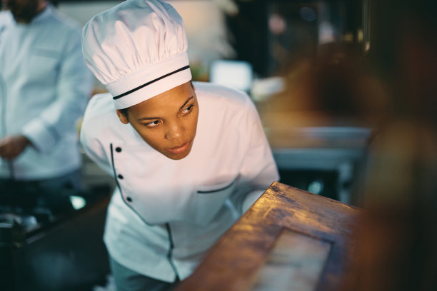 非裔美国专业厨师在餐馆工作时检查烤箱里的食物。图片下载