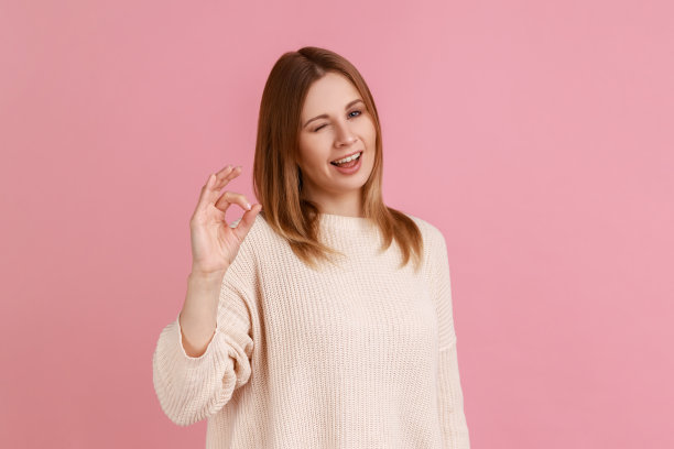 有吸引力的乐观金发女人的肖像看着相机显示ok手势和眨眼。图片下载