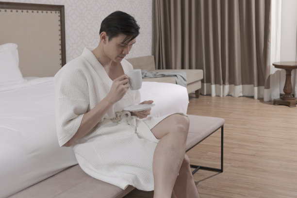 年轻男子穿着浴袍在卧室喝咖啡。男性早上喝咖啡。图片下载