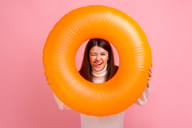 深色头发快乐的女人与顽皮的表情看槽橙色橡胶圈，显示舌头。图片下载