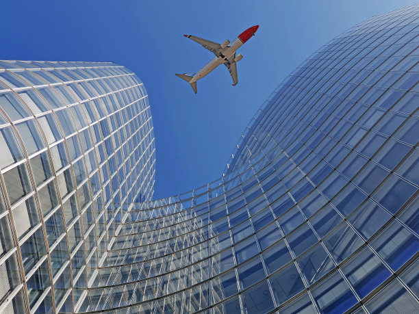 飞机飞越现代办公玻璃摩天大楼图片下载