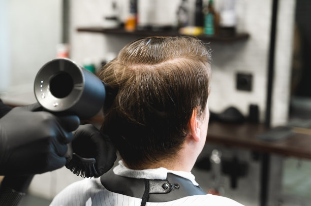 去理发店。年轻型男，商人做时尚发型。理发师、发型师、发型师用吹风机吹、吹头发，顾客和顾客坐在黑色的男士美容沙龙里，椅子上盖着一件披风图片下载