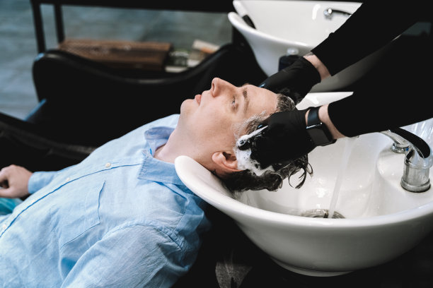 去理发店。年轻型男，商人做时尚发型。理发师，发型师，发型师用洗发香波和水槽里的香油洗头。黑色男士美容院，黑色椅子图片下载
