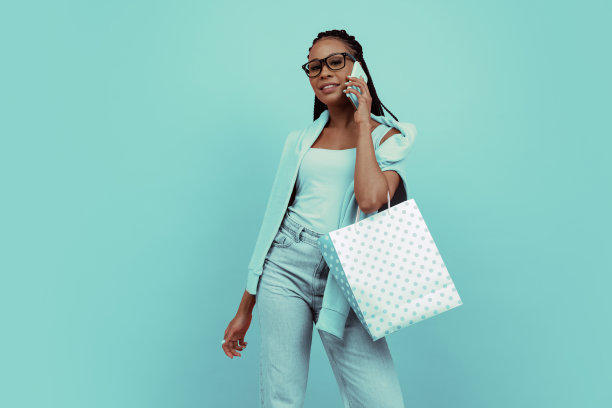 单色肖像年轻迷人的女孩与非洲发型持有购物袋孤立的蓝色背景。概念美，艺术，时尚，青春，风格图片下载