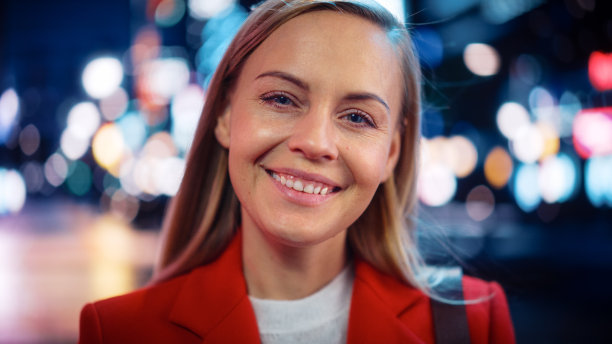 特写肖像美丽的白人妇女微笑，看着相机，站在夜晚的城市与散keh霓虹灯。快乐自信的年轻女性与金发和蓝眼睛。图片下载