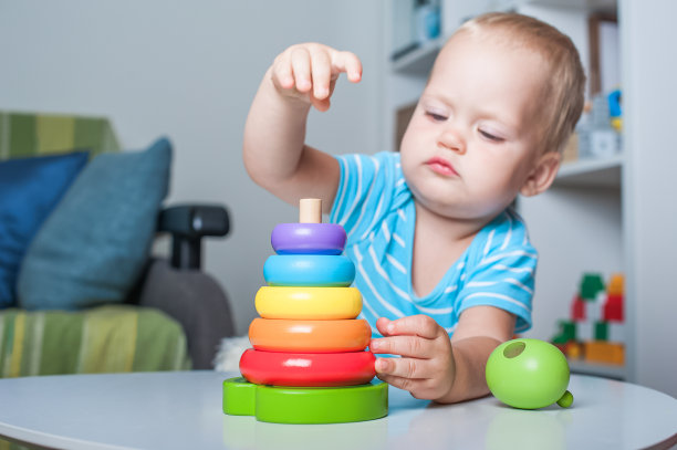 英俊的蹒跚学步的男孩在孩子的房间里玩木制和塑料玩具。图片下载