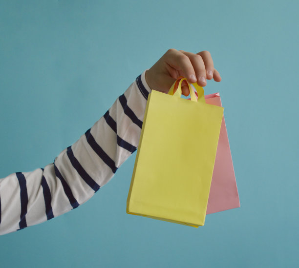 蓝色背景上一个孩子手握牛皮纸包的特写。生态包装的概念。图片下载