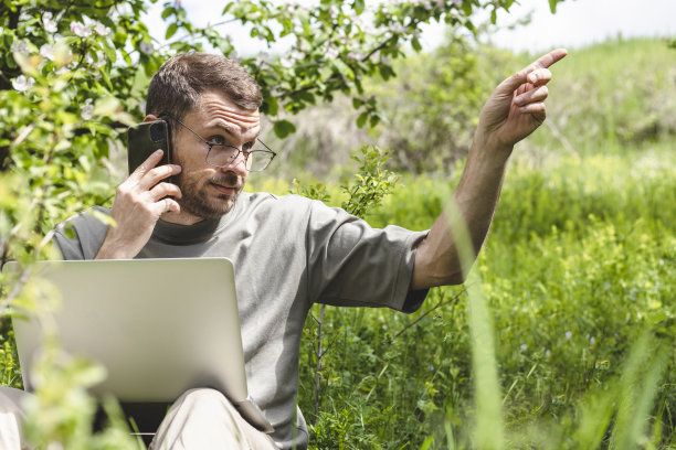 严肃的成年男子在户外工作时打电话，手指在一边。图片下载