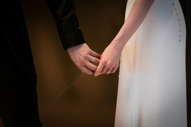 新婚夫妇手拿结婚戒指，穿着结婚礼服和西装。新婚夫妇戴着戒指的特写。图片下载