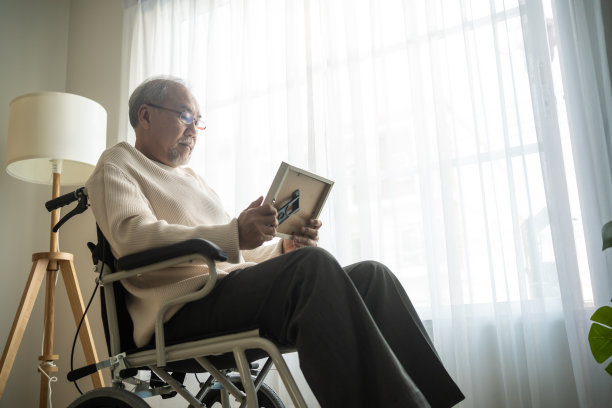 亚洲老年男性独自坐在轮椅上，看着家庭照片。年迈成熟的爷爷感到孤独和悲伤，在退休后呆在养老院想念他的亲戚和妻子。图片下载