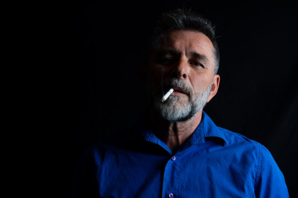 在黑色背景上吸烟的老年男性图片下载