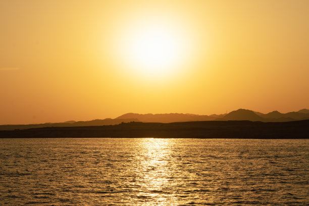 水平的形象。风景如画的明亮日落在彩色的蓝色和橙色的天空，埃及的沙漠山脉的剪影和海岸线的倒影在夏天晚上的海水度假。图片下载