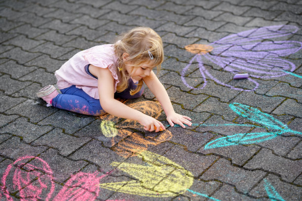 幼儿园的小女孩用彩色粉笔在后院的地上画花。积极快乐的蹒跚学步的孩子在沥青上画画和创造图片。夏季创造性的户外儿童活动。图片下载