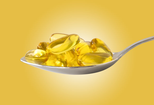 欧米伽-3鱼油胶囊放在银勺里，黄色背景图片下载