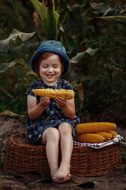快乐的小女孩拿着一穗玉米。图片下载