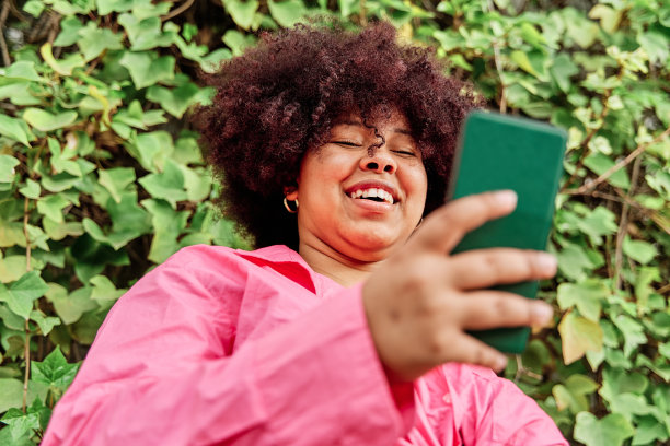 卷发的年轻女子在用她的智能手机。非裔美国女性使用社交媒体的肖像。图片下载