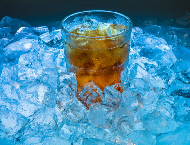 一个雾气弥漫的杯子里放着冰凉的金黄色饮料和冰块图片下载