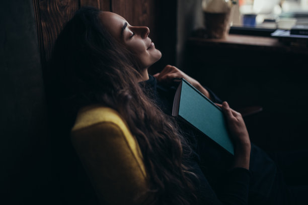 年轻漂亮的女人坐在扶手椅上看书。图片下载