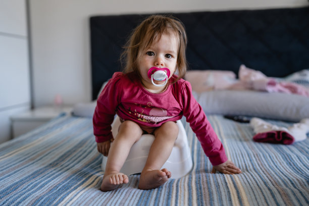 一名一岁的白人小女婴坐在儿童的便盆上在家里的床上，在白天全长奶嘴奶嘴在嘴前视图拷贝空间图片下载